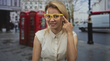 Sarı gözlüklü sarışın kadın güneşli şehir caddesinde baş parmak işareti yapıyor..