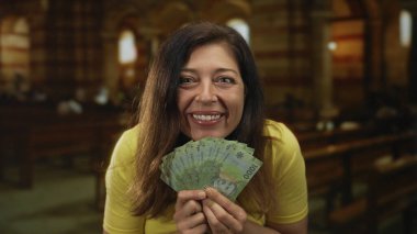 Orta yaşlı İspanyol kadın Şili pezosu banknotlarını klasik bir kilise nave içinde tutuyor; neşe cömertliği hayırseverlik umudu.