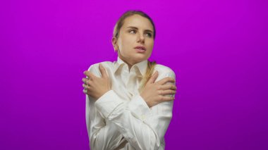 Kadın gergin bir şekilde pembe bir arkaplanda kendine sarılıyor. Yumuşak bir yüz ifadesi ve günlük beyaz gömleği kullanarak duygu ve yalnızlığı tasvir ediyor..