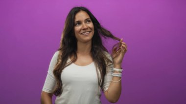 Mor stüdyo ortamında gülümseyen, dokunaklı saç ve bileklik takan genç İspanyol kadın..