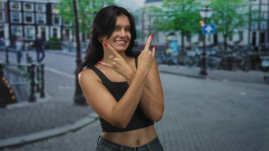 Siyah kolsuz bluz giyen kadın, sokak ortamında bisikletle kaplı taş boynuzlarını gösteriyor..