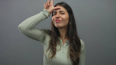 Genç İspanyol kadın stüdyo oturumunda gri bir duvara karşı el pençe divan duran ezik bir jest yapıyor. Alay ediyor..