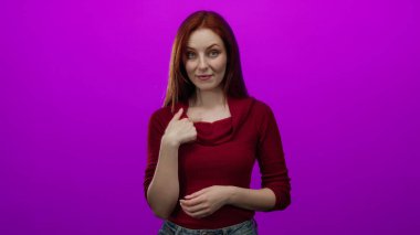 Kızıl saçlı kadın, parlak pembe bir arka plana karşı el kol hareketi yapar. Kendini tanıtır ve gülümseyerek inkar eder..