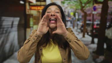 Orta yaşlı İspanyol bir kadın sokakta elleri sımsıkı bağlı bağırıyor; coşkulu bir ses ifadesi var..