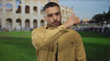 İnsan parmaklarını kaldırarak antik Roma kolezyum binasını işaret ediyor. Parlak gökyüzü altında detaylı bir cephe var..