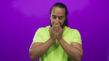 Yüzü elle kaplayan ve mor stüdyoda burnunu silen adam limonlu gömlek giyiyor, gözleri kapalı ve gergin duruş; rahatsızlık yorgunluğu yorgunluğu.