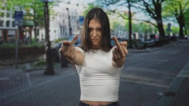Şehrin göbek deliği delme ve gergin yüz ifadesi olan bir caddesinde iki orta parmağı da kameraya doğru tutan kadın..