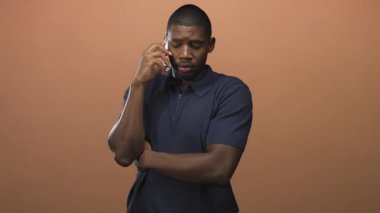 Akıllı telefonu kulağına doğru tutan genç bir adam. Gözleri kapalı, kaşları çatık. Stüdyoda şaşkın bir dinleme hareketi..