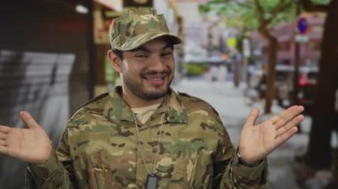 Kamuflaj üniformalı adam, mağazaların vitrinleri ve kaldırımların arasında elleri açık bir şekilde omuz silkiyor; belirsizlik içinde..