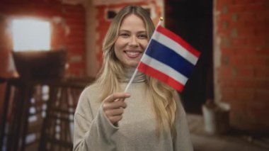Sarışın kadın gülümseyen Tayland bayrağını inşaat sahasında tutuyor. Vatansever gurur ve destek..