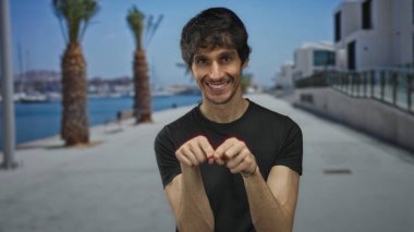 Siyah tişörtlü adam elleri ile kalp şekli yapar ve liman güvertesinde bir öpücük atar; romantik aşk.