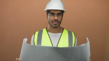 Adam kahverengi stüdyoda güvenlik yeleği ve beyaz şapka giyerken iki eliyle planı yuvarladı; stratejik planlama güveni.