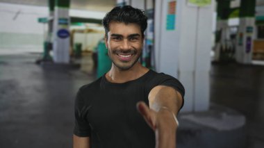 İspanyol adam gülümser ve sokaktaki kentsel benzin istasyonunda el sıkışmak için elini uzatır; güven bağlantısı.