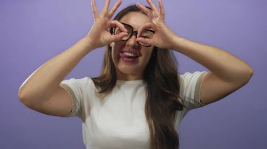 El dürbünü yapan kadın mor stüdyoda gülümserken gözlerinin etrafına jest yapıyor ve gülüyor..