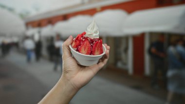 Şehrin kalabalık bir caddesinde elinde lezzetli bir fincan çilekli dondurma tutan erkek. Bulanık insanlar yürüyor. Canlı şehir hayatı ve yaz ziyafetleri sergiliyorlar..
