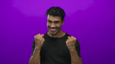 Siyah gömlekli genç İspanyol adam canlı mor stüdyo ışıklandırması altında yumruklarını sıkar ve dişlerini gıcırdatır. Zafer zaferini kutlar..