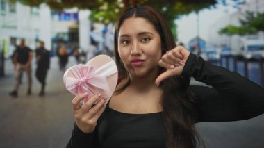 Kalabalık şehir caddesinde elinde saten kurdeleyle pembe kalp kutusu tutan genç İspanyol kadın reddediyor;.
