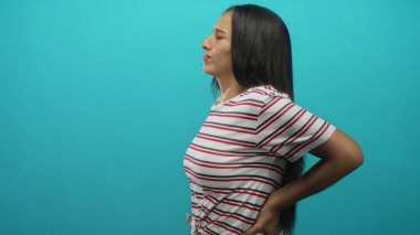 Sırtında eli, sırtında çizgili tişörtü olan İspanyol genç bir kadın. Stüdyoda acı çeken bir ifade. Sırt ağrısı..