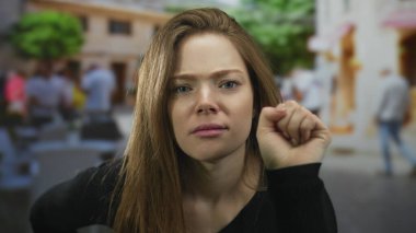 Kahverengi saçlı genç bir kadın kalabalık bir caddenin köşesinde kameraya doğru eğiliyor..