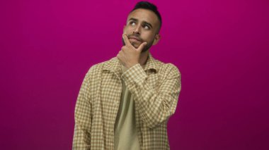 Genç İspanyol adam çenesine dokunuyor ve stüdyoda eflatun duvarla işaret ediyor. Düşünceli bir yansıma..