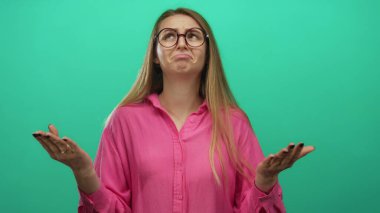 Pembe gömlekli genç bir kadın, izole edilmiş yeşil arka plan duvarına karşı anlamlı bir şekilde hareket ediyor..