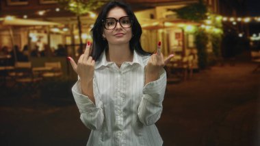Beyaz çizgili gömlek ve gözlüklü genç İspanyol kadın sokak kafesinin terasında dikilirken orta parmağını kaldırıyor..