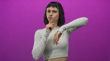 Latin kökenli genç bir kadın mor stüdyo duvarına parmak işareti yapıyor. Zaman kontrolü yapıyor. Sabırsızlık..