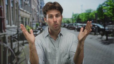 Şehirde, park halindeki arabalar ve bisikletlerin arasında elini kolunu sallayarak el kol hareketi yapan genç bir İspanyol..