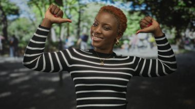 Genç Afro-Amerikalı kadın, hareketli şehir sokak gündüz sahnesinde iki başparmağını da göğsüne işaret ediyor..