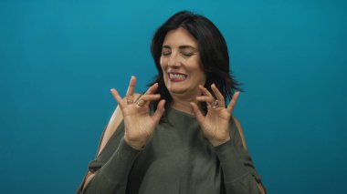 Orta yaşlı bir kadın stüdyo ortamında ürkek bir ifadeyle kameraya doğru geri çekiliyor..