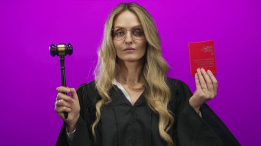 Yargıç üniformalı genç sarışın kadın İsviçre pasaportu ve münferit pembe arka planda tokmak taşıyor..