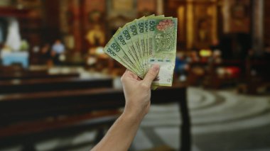 Kilise ortamında arjantinli pezolarla el ele tutuşmak, paranın altını çizmek, erkek eli, arjantinli para birimi ve bulanık sıraları ve sunağı olan kapalı bir dini ortam..
