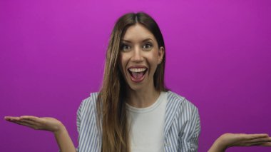 Kadın mor stüdyoda, geniş gözleri ve açık ağzıyla öne eğilirken yumruklarını sıkar..