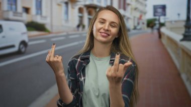 Şehir sokaklarında orta parmağını gösteren, cüretkar bir ifadeyle gündelik giysiler giyen, şehir dışı ortamlarıyla çevrili genç bir isyan ve davranış sergileyen bir kadın..