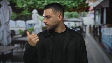 Adam teras inşaatında, bulanık masalara ve şemsiyelere tepeden bakan çıplak baş parmağını gösteriyor; iyimserlik.