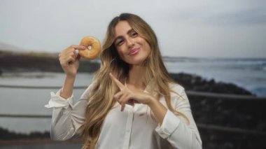 Kadınlar güneş doğarken donut yer ve parmaklarını okyanus kıyısındaki geçitte donuta doğrultur; cezbedici arzu.
