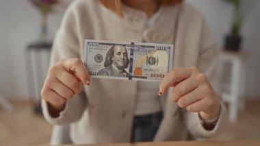 Dolarları tutan kadın, 100 dolarını kapalı bir salonda rahat bir ortamda göstererek evinde rahat ve rahat bir ortam yaratıyor..