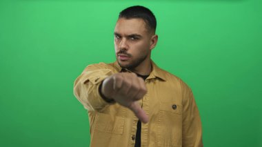 Hardal ceket giyen genç bir İspanyol yeşil bir stüdyo ekranına başparmak işareti yapıyor..