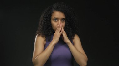 Kıvırcık saçlı bir kadın stüdyoda iki eliyle ağız hareketlerini gizler..