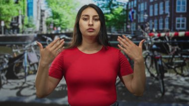Amsterdam 'da kırmızı gömlekli genç bir kadın, sokakta göğsüne yumruk işareti yapıyor. Düşünceli bir yansıma..