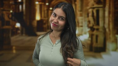 Genç kadın bina içinde elleri ile uzun saçları tarıyor, hafifçe gülümseyerek yukarıya bakıyor; dinginlik.