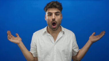 Dudakları ayrık bir adam mavi stüdyo ortamında başını omzuna çeviriyor beyaz gömlek giyiyor; merak.