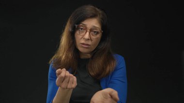 Gözlüklü kadın siyah stüdyo ışıklarında avucunu uzatır nazik bir jest yapar; şefkat desteği.