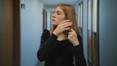 Otel koridorunda stresli bir kadın, sarı saçlı ve siyah giyinmiş, endişeli bir yüz ifadesi sergiliyor..