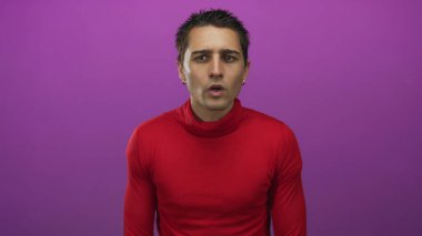 Kırmızı tişörtlü genç İspanyol adam, izole edilmiş mor arka plan duvarına karşı duruyor ve duygularını ifade ediyor.