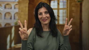 Gülümseyen İspanyol kadın, üniversite binasında parmaklarıyla barış işareti gösteriyor. Sıcak güneş ışığıyla yıkanmış, barış sevinci..