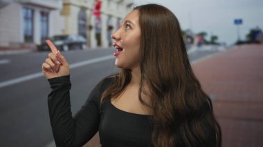 Genç İspanyol kadın şehir binasının önündeki caddeyi işaret ediyor. Gözleri yukarı bakıyor. Meraklı bir keşif..