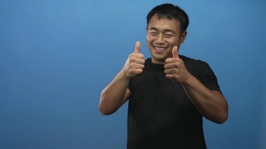 Siyah tişört giyen genç Çinli adam işaret parmağıyla mavi stüdyo ortamındaki izleyiciyi işaret ediyor..