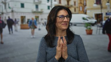 Güneşli şehir caddesinde ellerini sımsıkı bağlayıp dua eden bir kadın duruyor ve nazikçe gülümsüyor:.