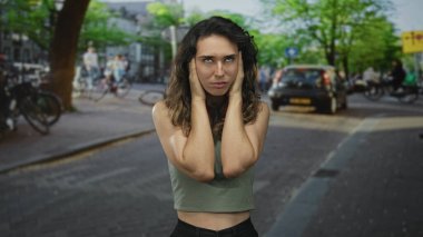 Sokak trafiğinin yoğunlaştığı ve bisikletlerin geçtiği bir ortamda İspanyol genç kadın kulaklarıyla kulaklarını tıkıyor; gürültü bunalımı.